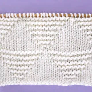 Knitted Stacked Triangle Stitch Pattern texture in white yarn on knitting needle.
