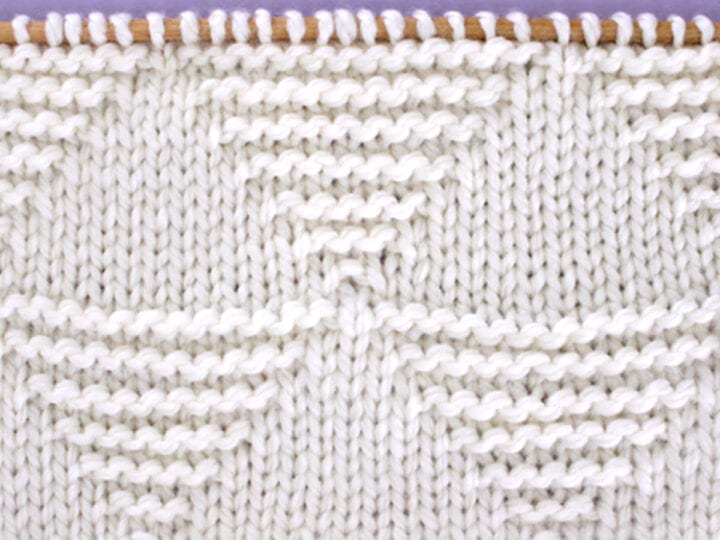 Knitted Stacked Triangle Stitch Pattern texture in white yarn on knitting needle.