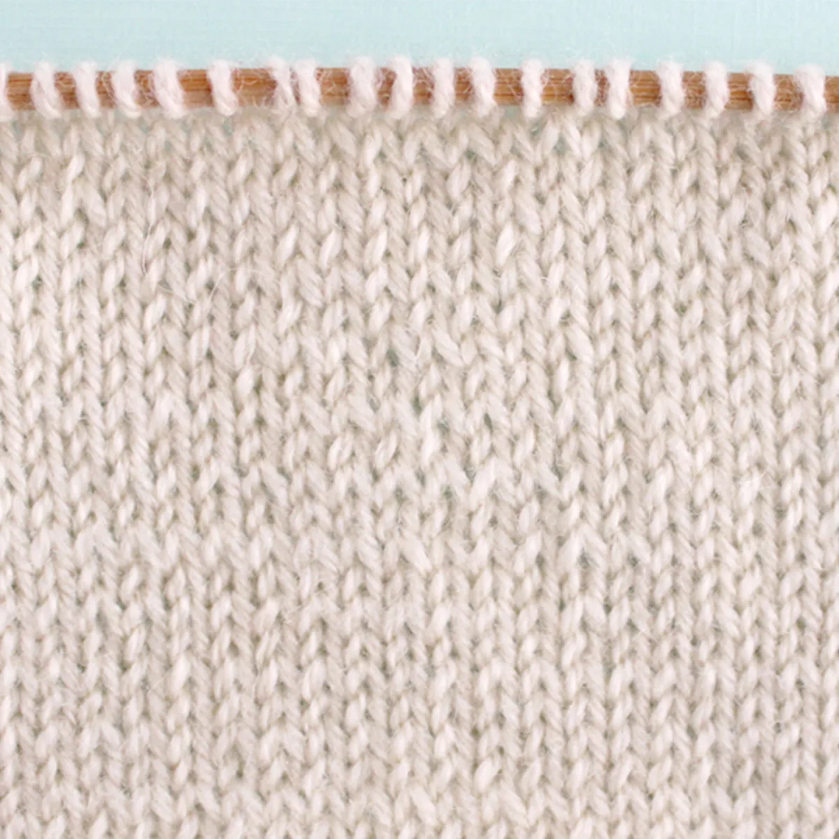Stockinette Knit Stitch Pattern texture in white color yarn on knitting needle.