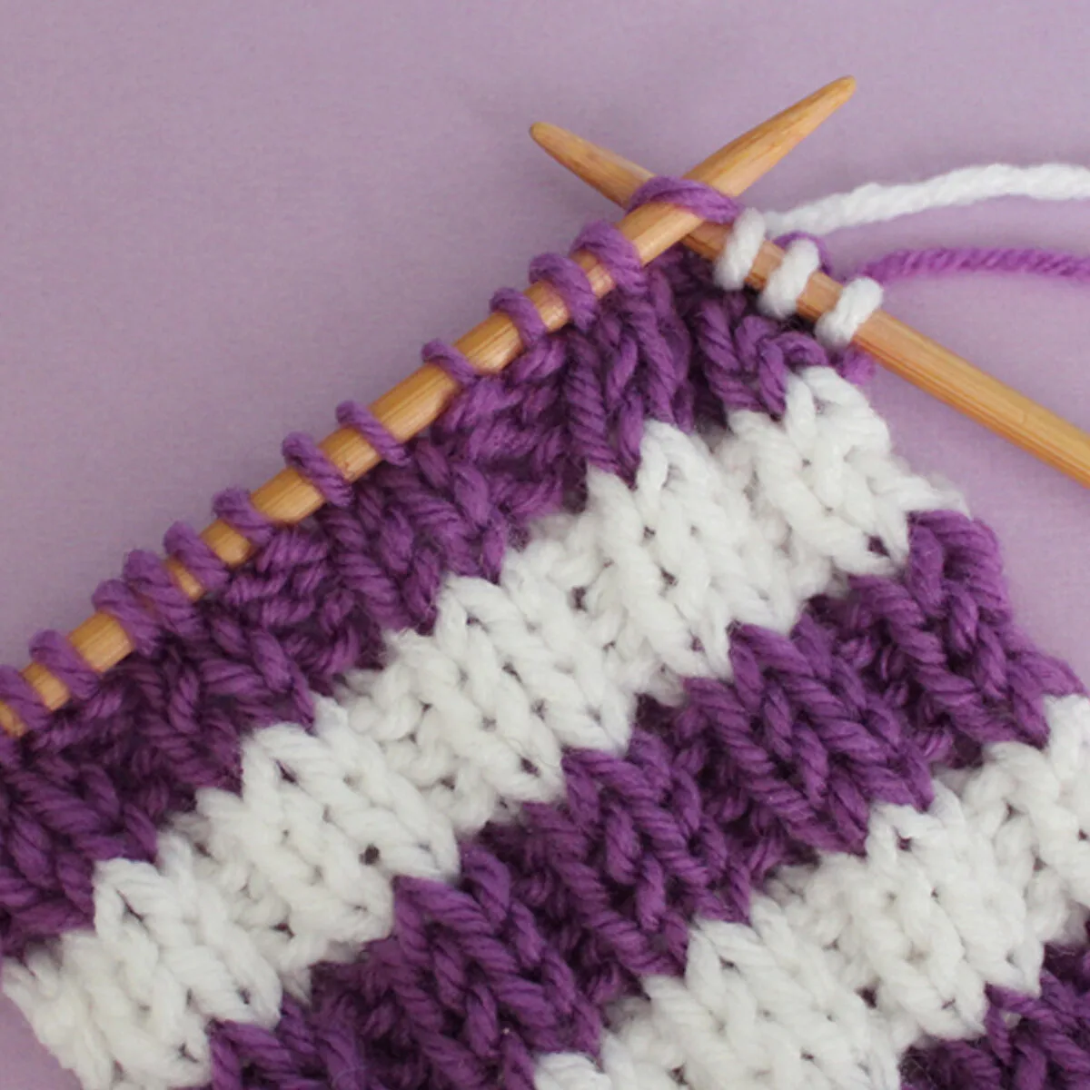 Knitted Stripes in rib stitch pattern with purple and white yarn colors on knitting needles.