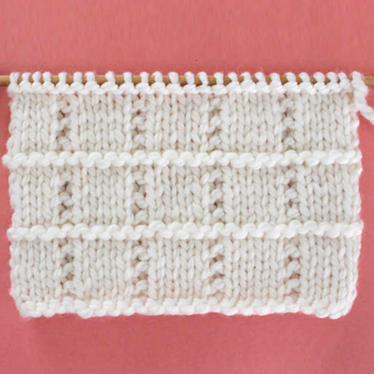 Tile Squares Knit Stitch Pattern in white yarn on knitting needle.