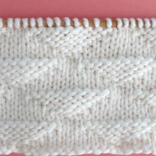 Pique Triangle Knit Stitch Pattern in white yarn on knitting needle.