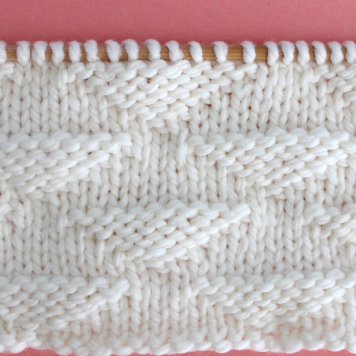 Pique Triangle Knit Stitch Pattern in white yarn on knitting needle.