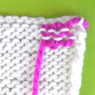 Yarn ends woven into a white knit swatch demonstrated by bright pink yarn.