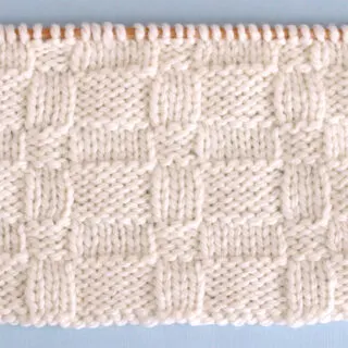 Knitted Wide Basket Weave Stitch Pattern in white yarn on knitting needle.
