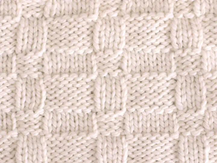 Knitted Wide Basket Weave Stitch Pattern in white yarn on knitting needle.