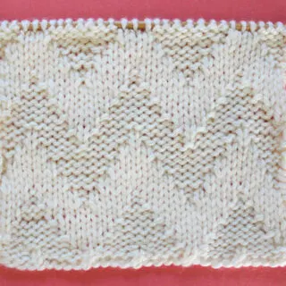 Knitted Wide Chevron Stitch Pattern in white yarn on knitting needle.