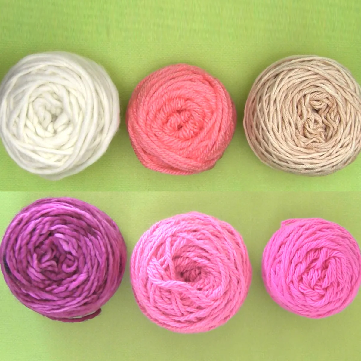 Six yarn balls in purple, pink, and white yarn colors arranged atop a green background.