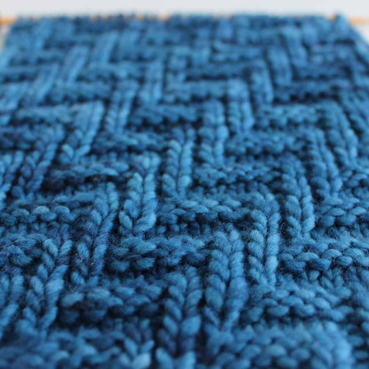 Diagonal Chevron Zigzag Knit Stitch Pattern in blue yarn on knitting needle.