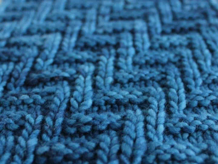 Diagonal Chevron Zigzag Knit Stitch Pattern in blue yarn on knitting needle.