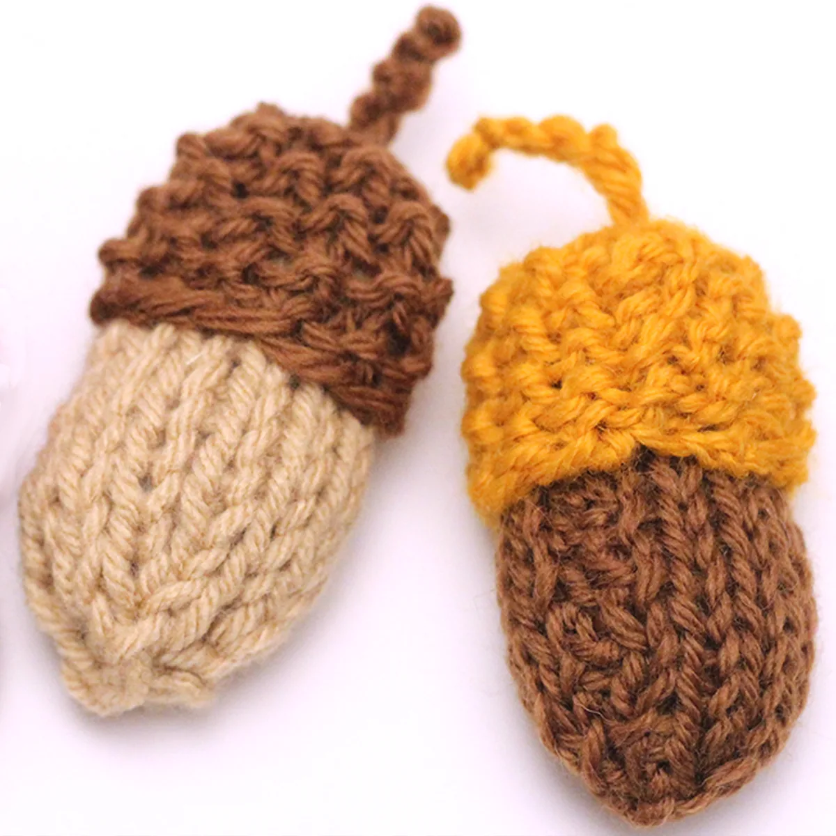 Two knitted acorn softies in brown, yellow, and beige yarn colors on a white background.