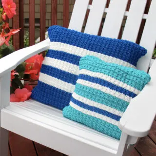 Two knitted pillows in hurdle stitch texture in shades of blue yarn color on a white adirondack chair.