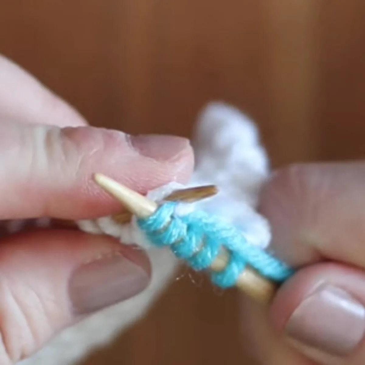 Hands demonstrating how to knit back with knitting needles and yarn.