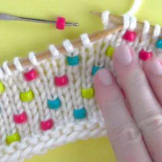 Knitted swatch in white yarn with beads inserted vertically and hand.