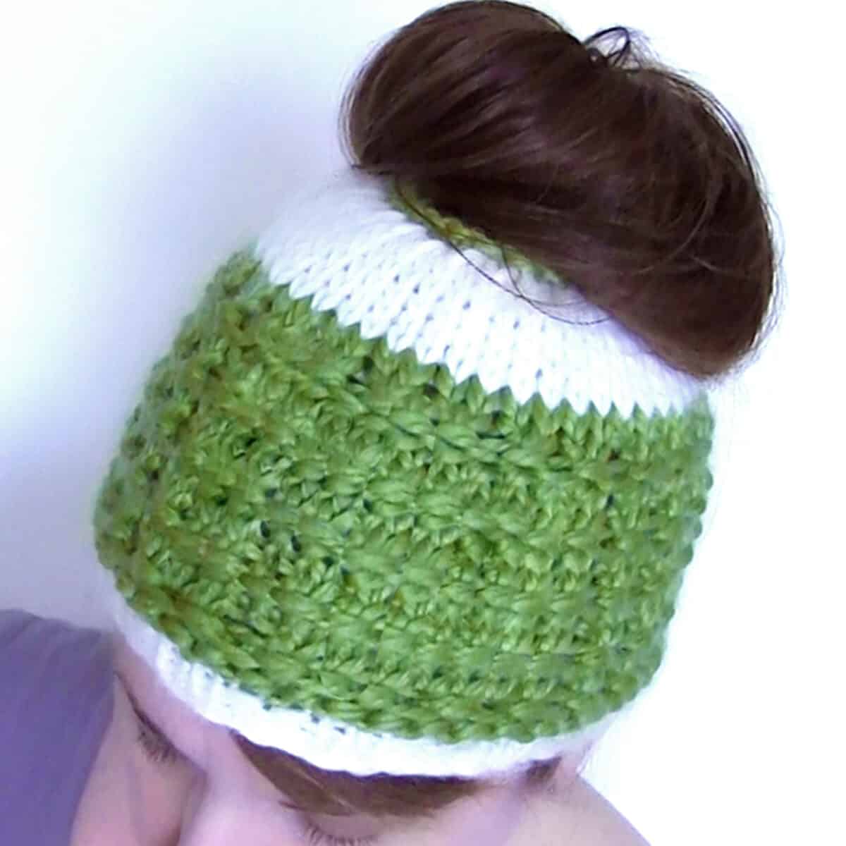 Woman wearing knitted Messy Bun Hat in green and white colored yarn with hair piled atop head.