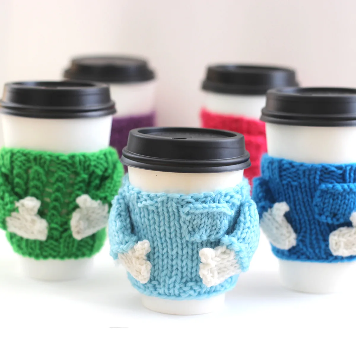 Take Out Coffee Cups with knitted sweater designed mug cozies in various colors.