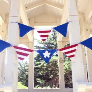 Knitted pennant banner in patriotic USA colors of red, white, and blue strung within a white gazebo.