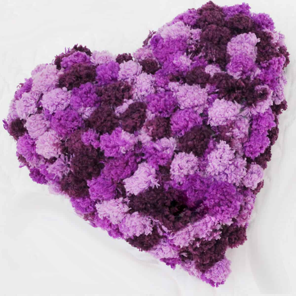 Knitted heart shaped pillow in pom pom yarn in shades of purple yarn color.