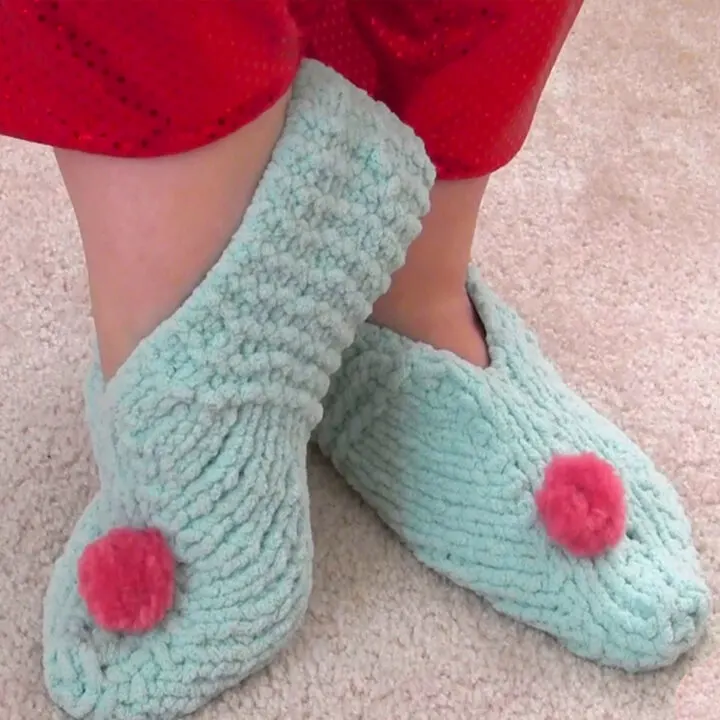 Knitted slippers in light blue yarn color with pink pom poms.