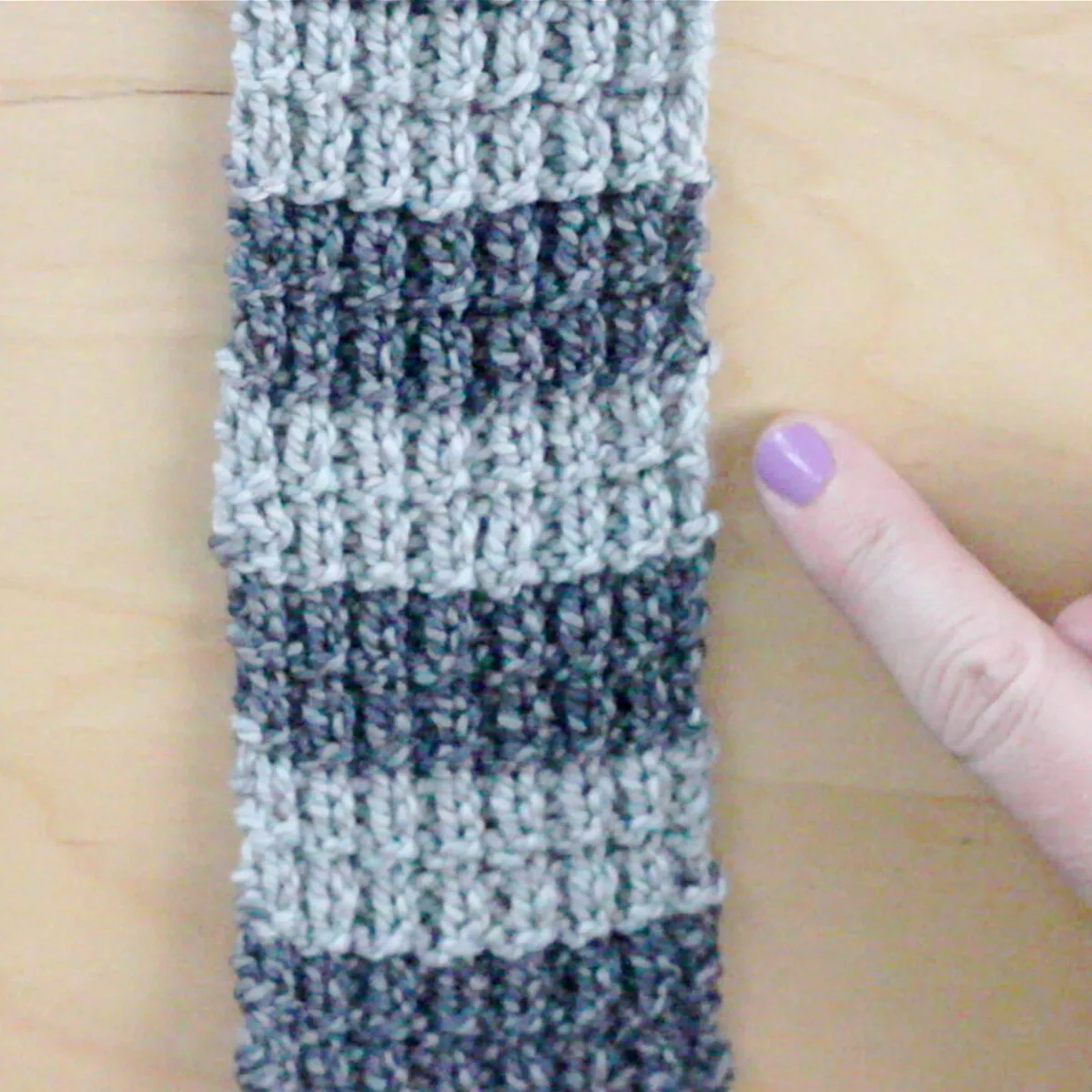 Knitted swatch in gray colored horizontal stripes with woman's hand.