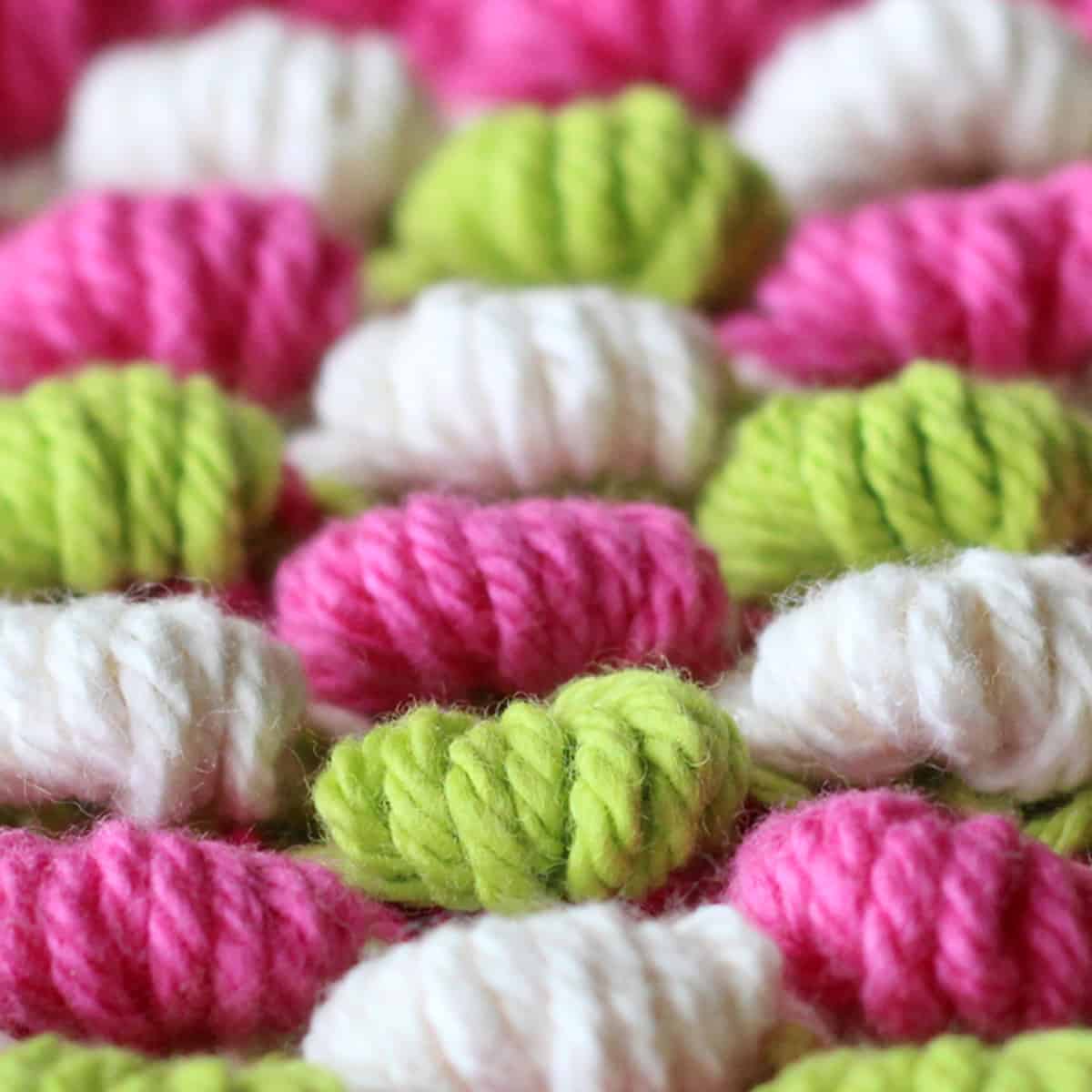 Spring Bobble Stitch Knitting Pattern texture in alternating green, pink, and white colors of yarn.