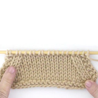 Hands pointing at knitted swatch to demonstrate increase and decrease techniques.