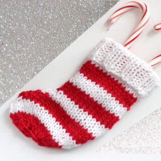 Knitted mini Christmas Stocking in alternating horizontal stripes in red and white yarn with candy canes inside.