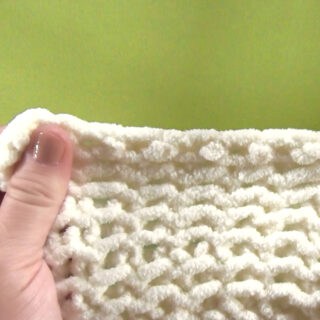 Hand holding a swatch of knitting to demonstrate the stretchy bind off technique.