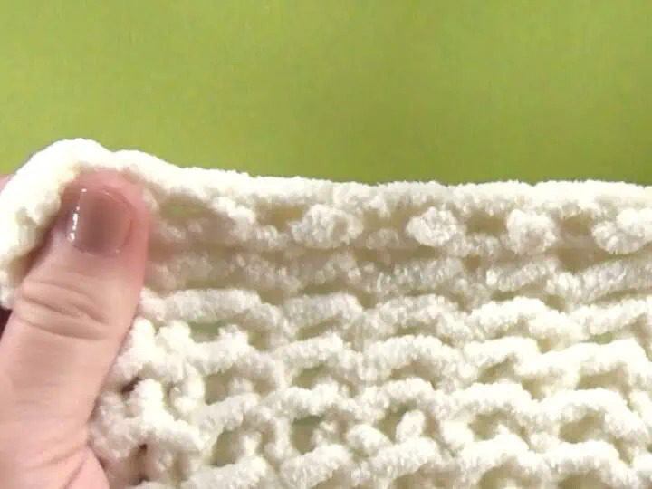 Hand holding a swatch of knitting to demonstrate the stretchy bind off technique.