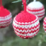 Knitted Christmas Ball Ornaments in red and white yarn colors hanging from outdoor greenery branches.