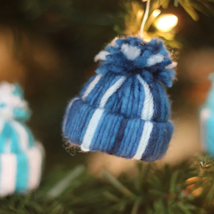 Yarn Hat holiday ornament in blue and white stripes hanging with Christmas tree.