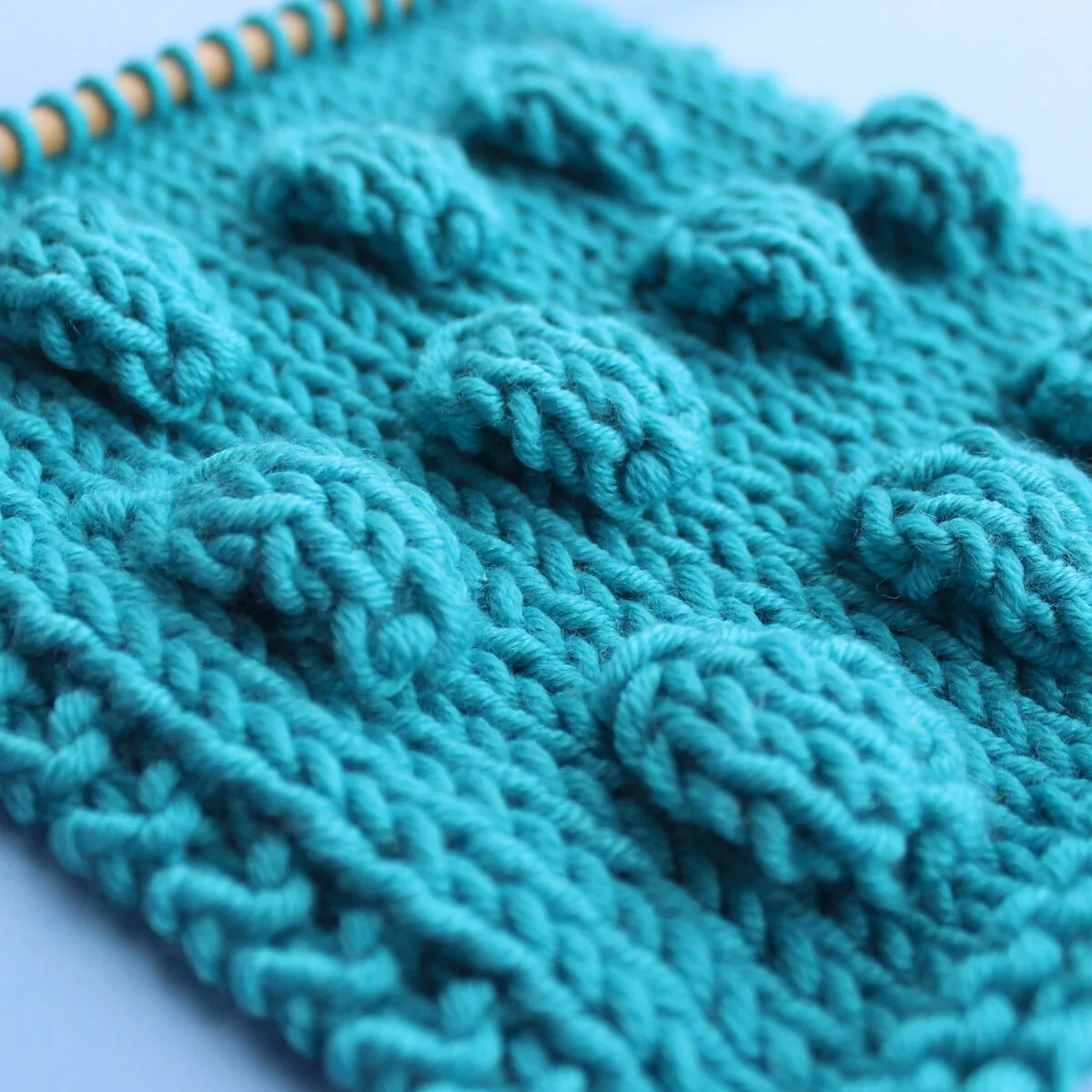 Side angle of Bobbles in Stockinette Stitch on knitting needle in blue color yarn.