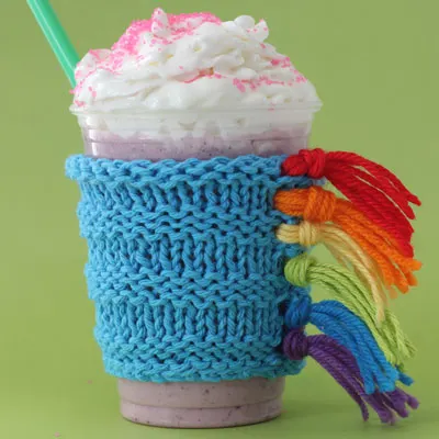 Knitted drink cozy in colorful unicorn design with fringe mane.