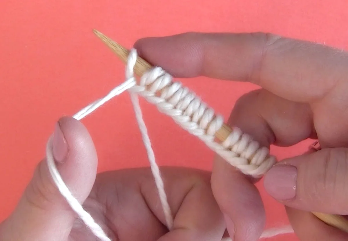 Hands casting on stitches onto a knitting needle with white color yarn.