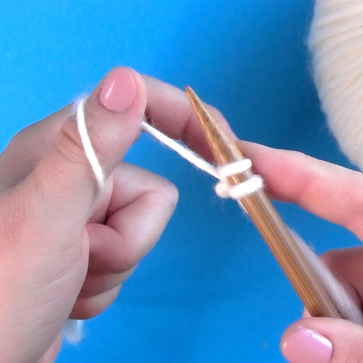 Casting on the thumb method with yarn and a knitting needle held by two hands.
