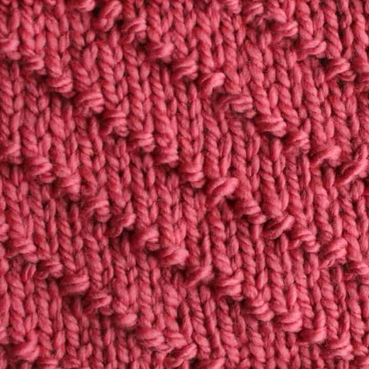 Diagonal Seed Knit Stitch Pattern in white yarn on knitting needle.