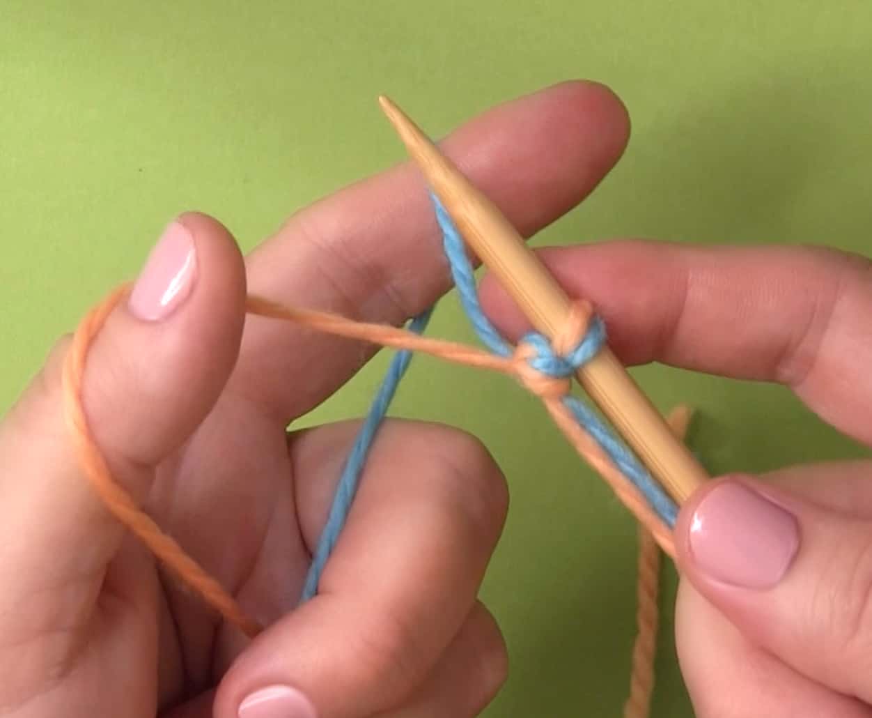 Hands holding one knitting needle with two yarn colors in the slingshot hold.