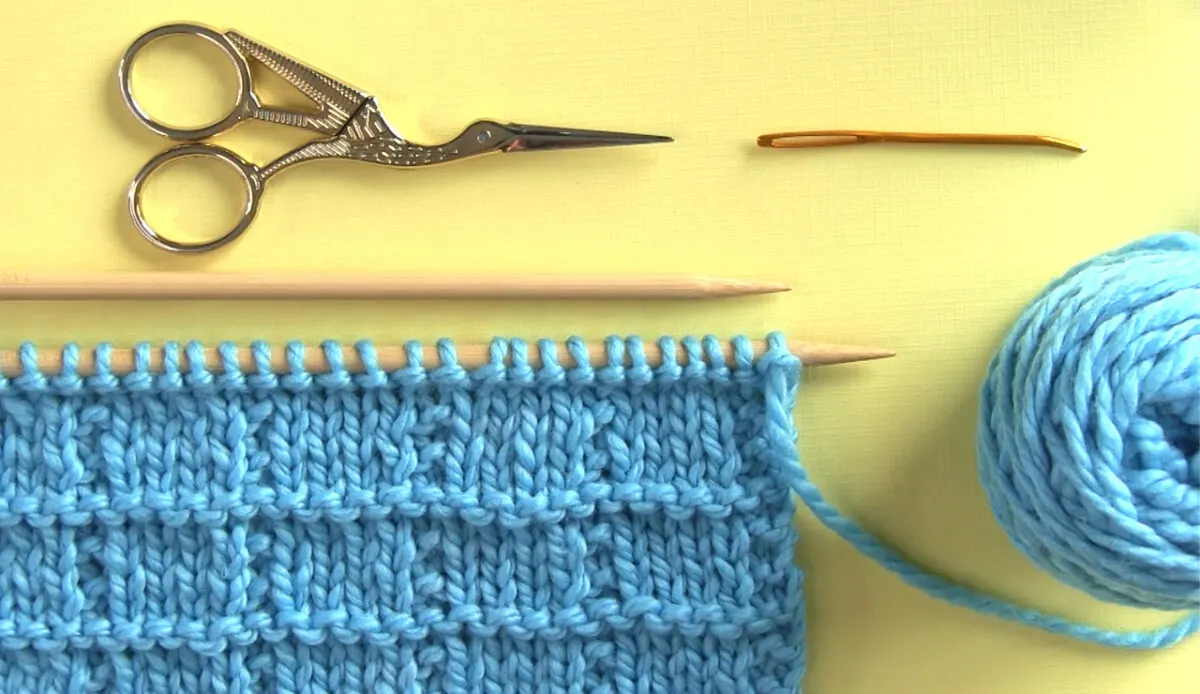 Knitted swatch of Tile Squares texture with knitting needles, scissors, yarn, and a tapestry needle.