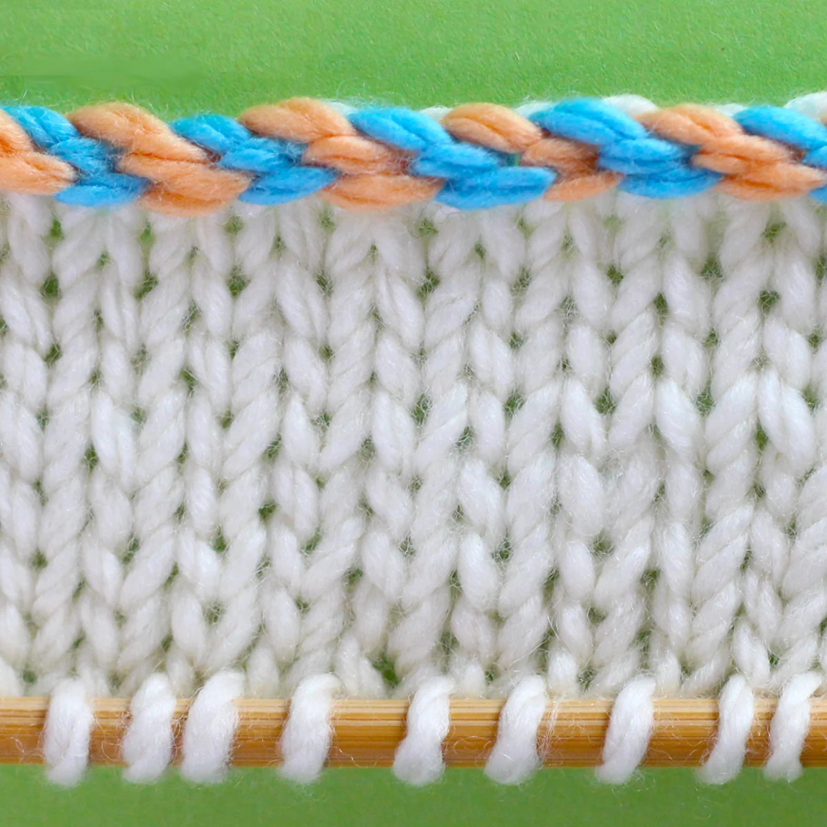 Knitted Swatch of stockinette with the edge in a 2-color braided cast on technique.