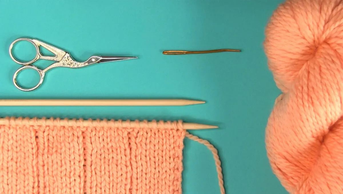 Knitting materials with knitting needles, yarn, scissors, and tapestry needle.