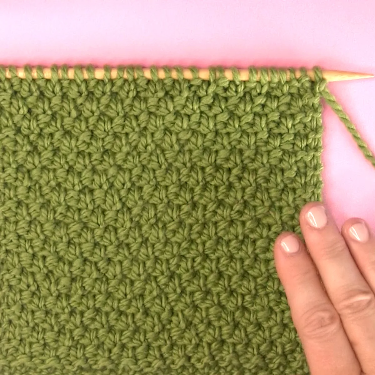 Irish Moss Knit Stitch pattern on knitting needle in green color yarn with woman's hand.