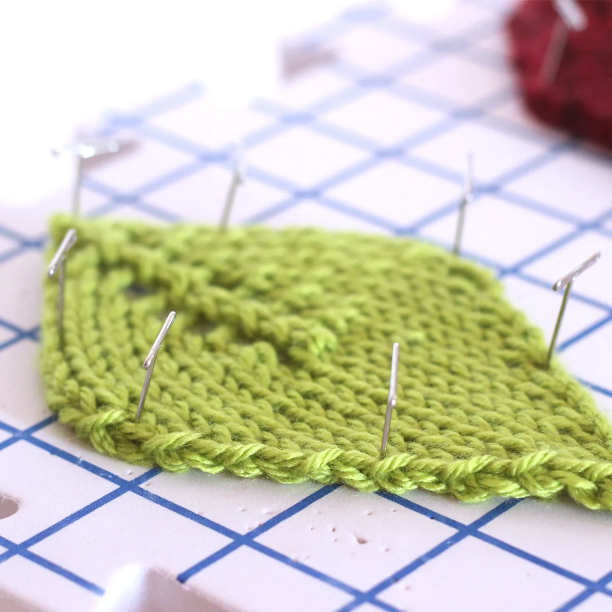 Green knitted leaf shape on a blocking mat with pins.
