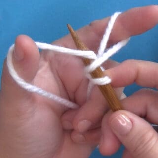 Hands demonstrating How to Long Tail Cast On Purlwise with yarn and knitting needles.
