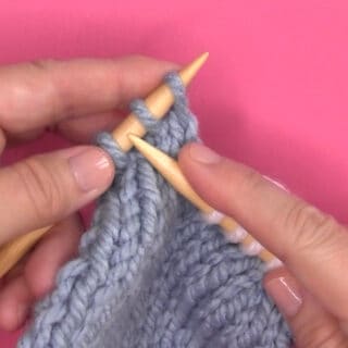 Demonstration of knitting two stitches together with needles, yarn, and hands.