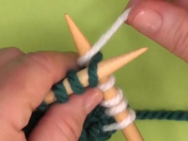 Demonstration of the KTBL Knit Through the Back Loop technique with hands, yarn, and needles.