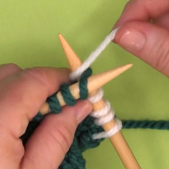 Demonstration of the KTBL Knit Through the Back Loop technique with hands, yarn, and needles.