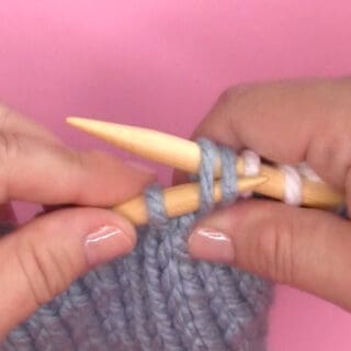 Demonstration of hands SSK knitting decrease technique with needles and yarn.
