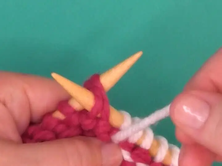 Demonstration of purl two together knitting technique with yarn, needles, and hands.