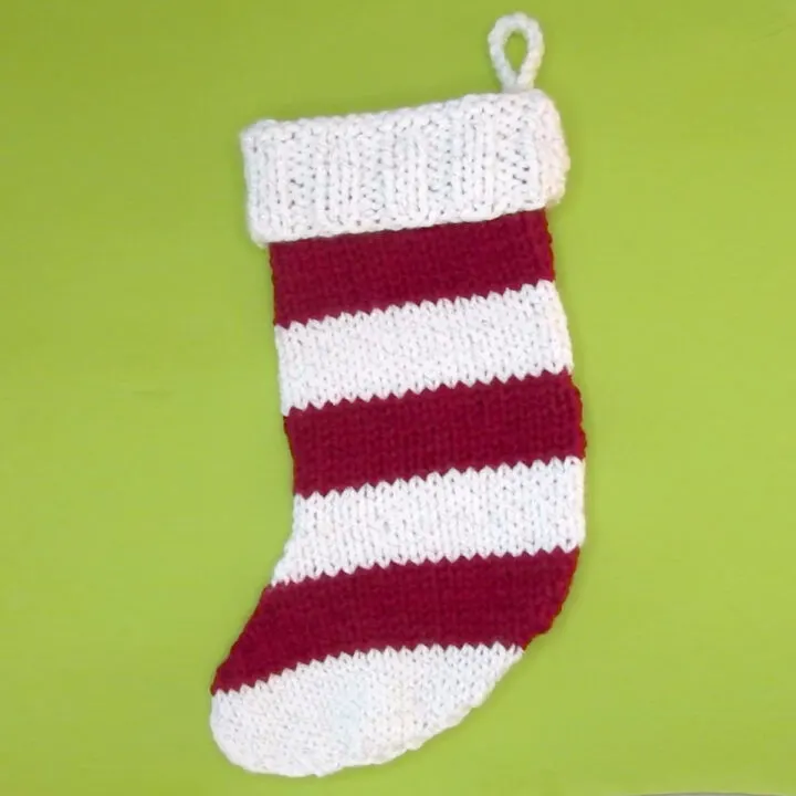 Knitted Christmas Stocking with red and white stripes on a green background.