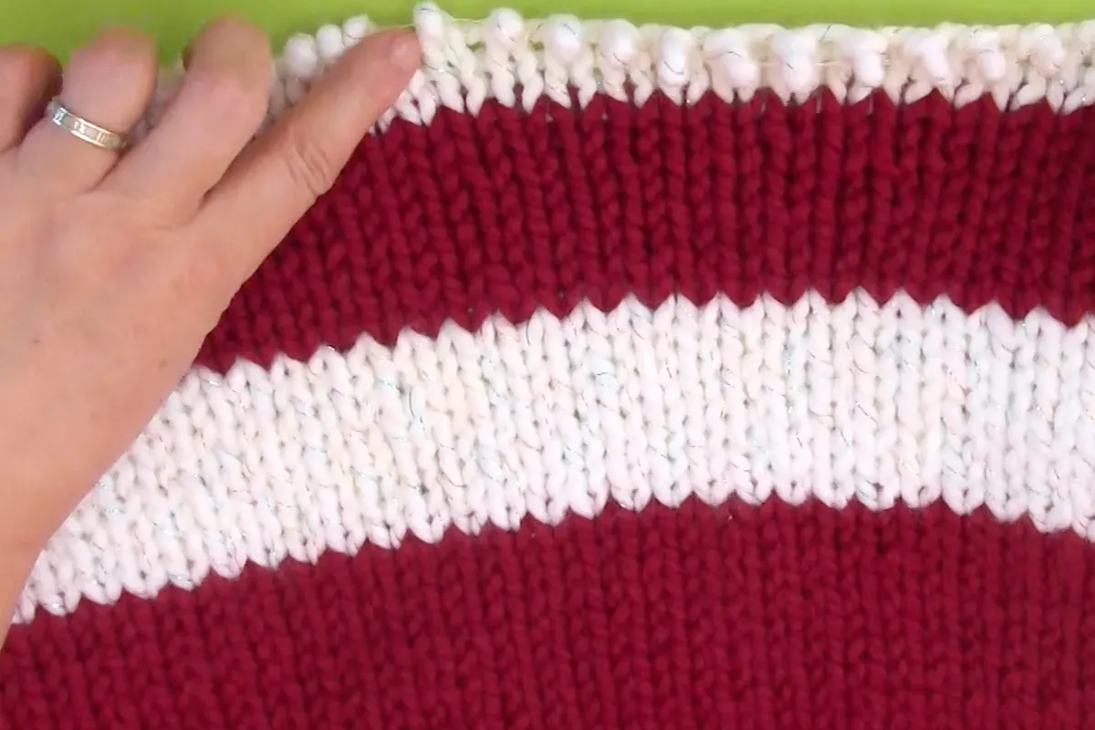 Red and white stripes knitted in Stockinette stitch on knitting needle.